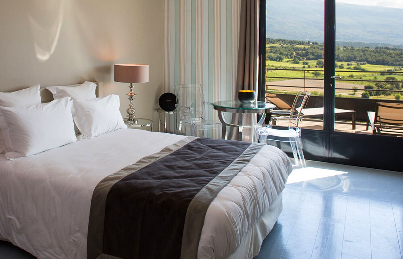 Ett hotellrum med en stor säng, ett glasbord och utsikt över landsbygden.