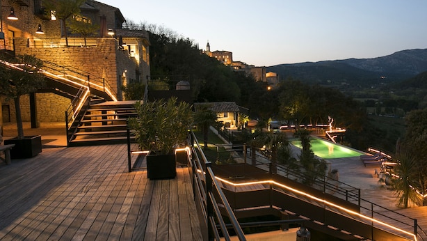 Une terrasse en bois avec une piscine, des murs en pierre et une vue sur le paysage environnant.