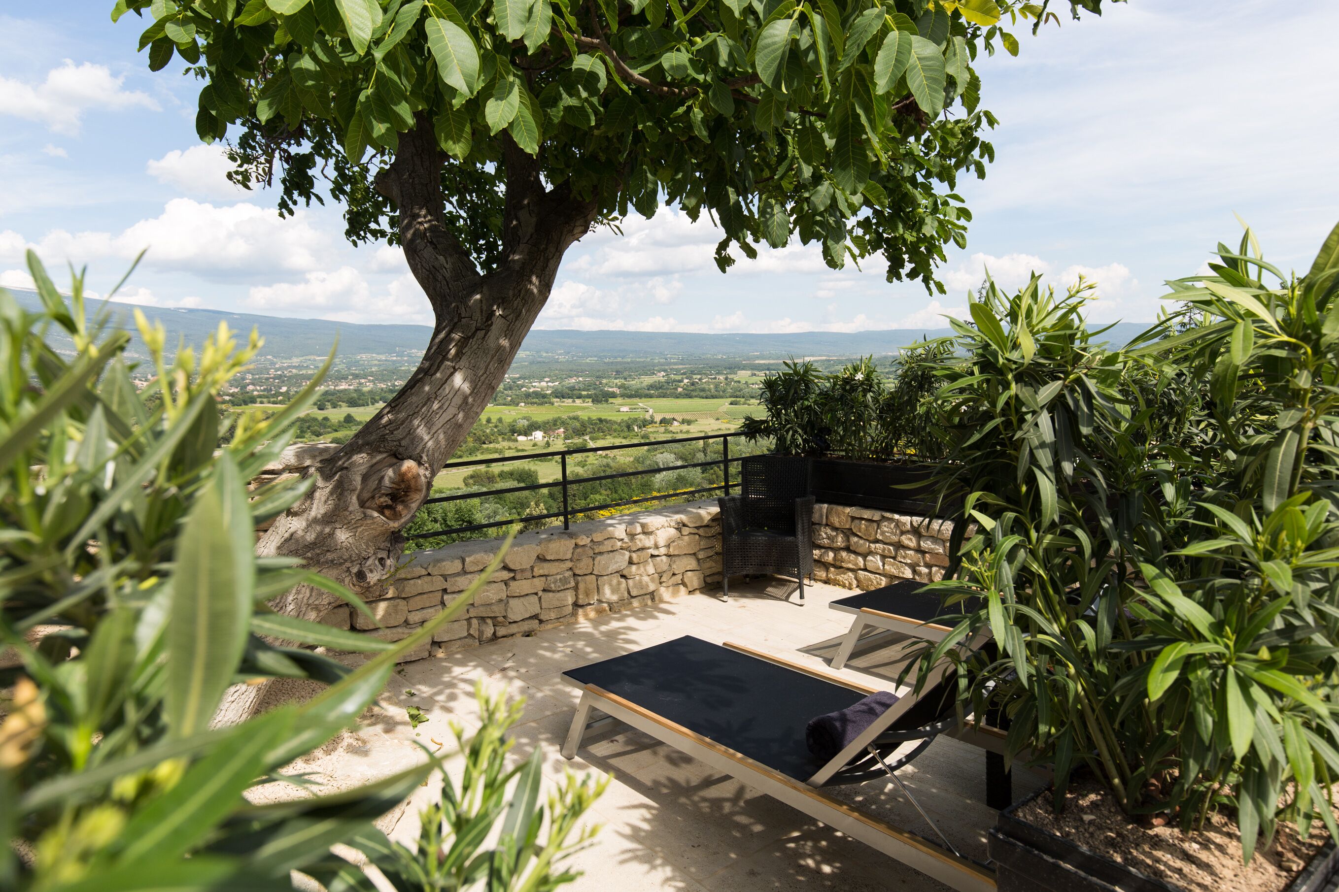 Eine Terrasse mit zwei Liegestühlen, einer Steinmauer und Blick auf eine Landschaft mit einem Baum und sanften Hügeln in der Ferne.