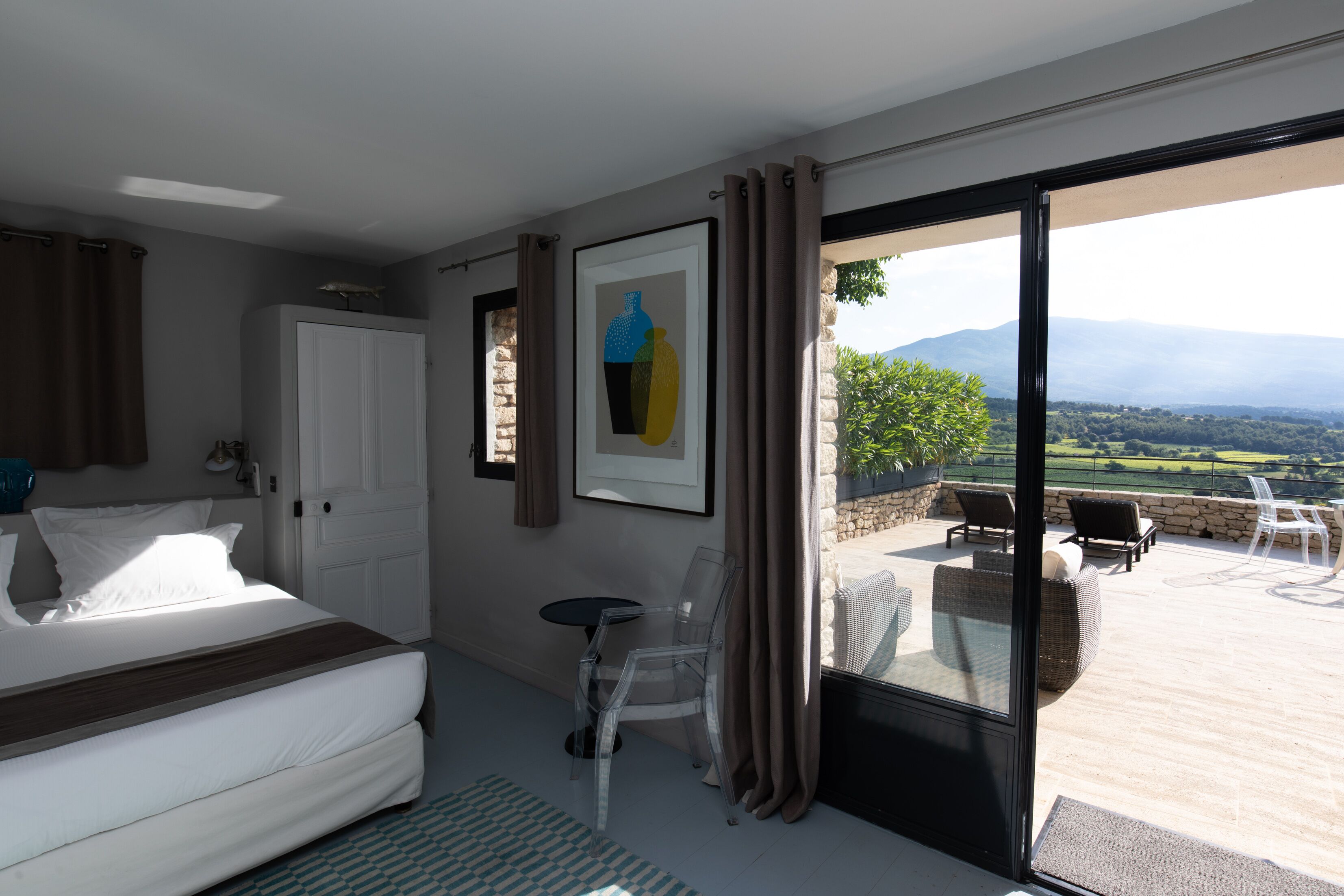 A bedroom with a bed, a small table, and chairs, a door, and a view of the outdoors.