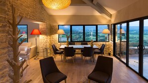 Un vaste espace dédié à la salle à manger, avec une grande table et des chaises, un mur en pierre et une vue sur la campagne grâce à de grandes fenêtres.