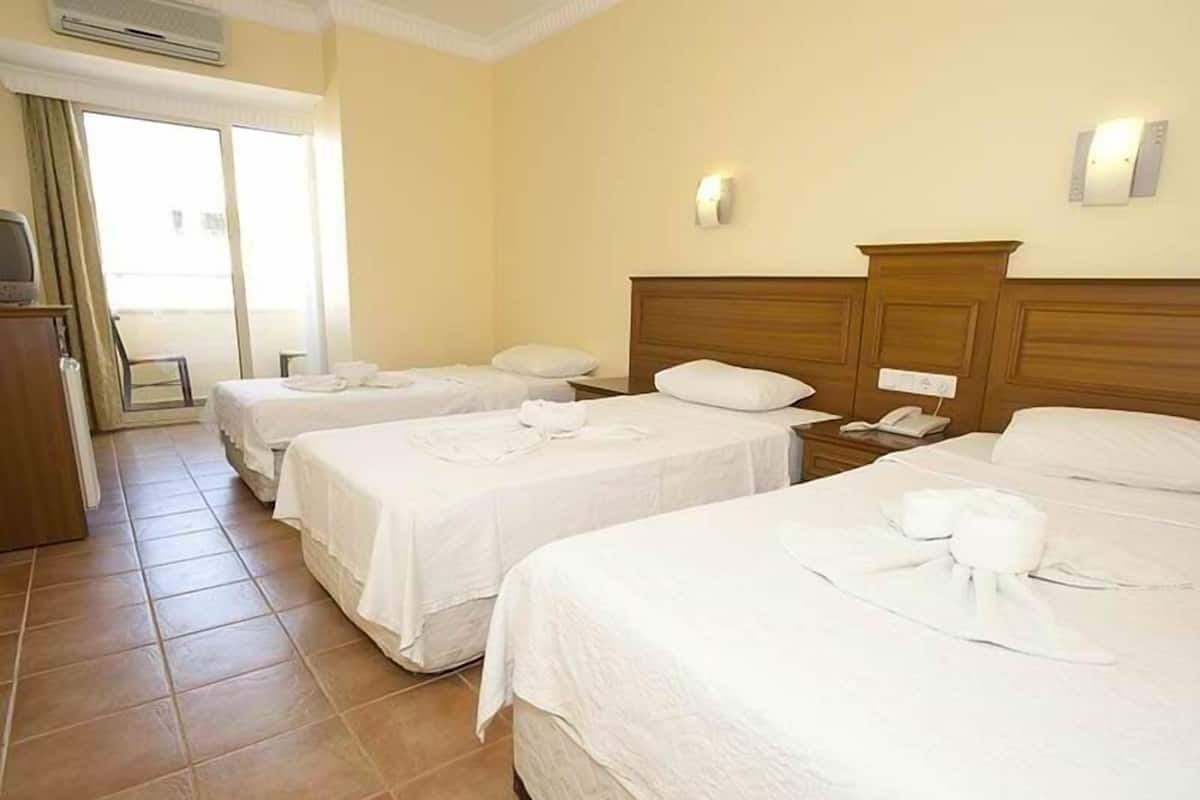 A hotel room with three single beds, a wooden headboard, a bedside table with a phone, and a small desk with a chair.