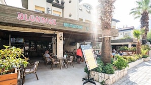 An outdoor seating area of a restaurant named 'Blondies Restaurant' with tables and chairs, surrounded by plants and palm trees.
