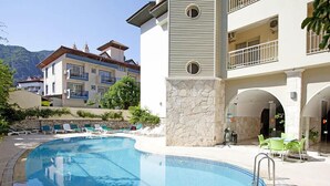 A swimming pool with lounge chairs, a stone wall, and a building with balconies.