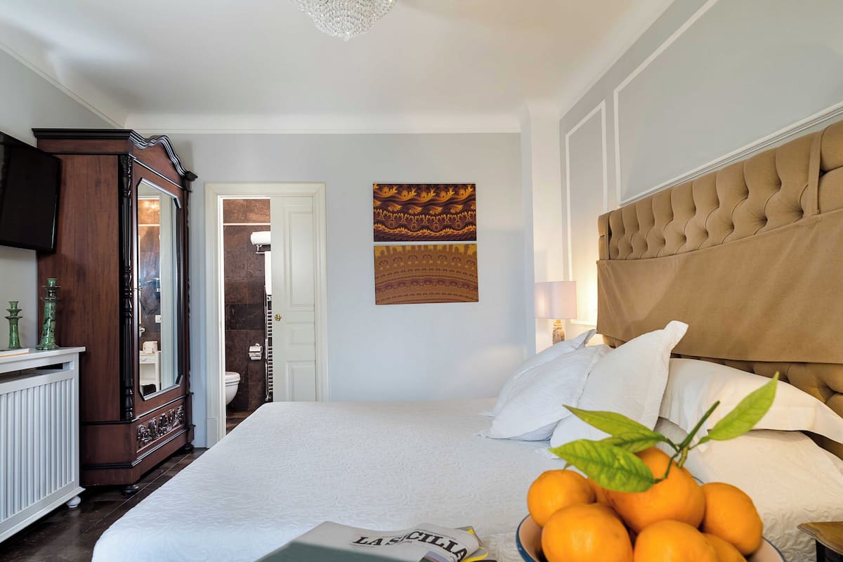 A bedroom with a bed, a dresser, a mirror, a wall-mounted artwork, and a door leading to another room.