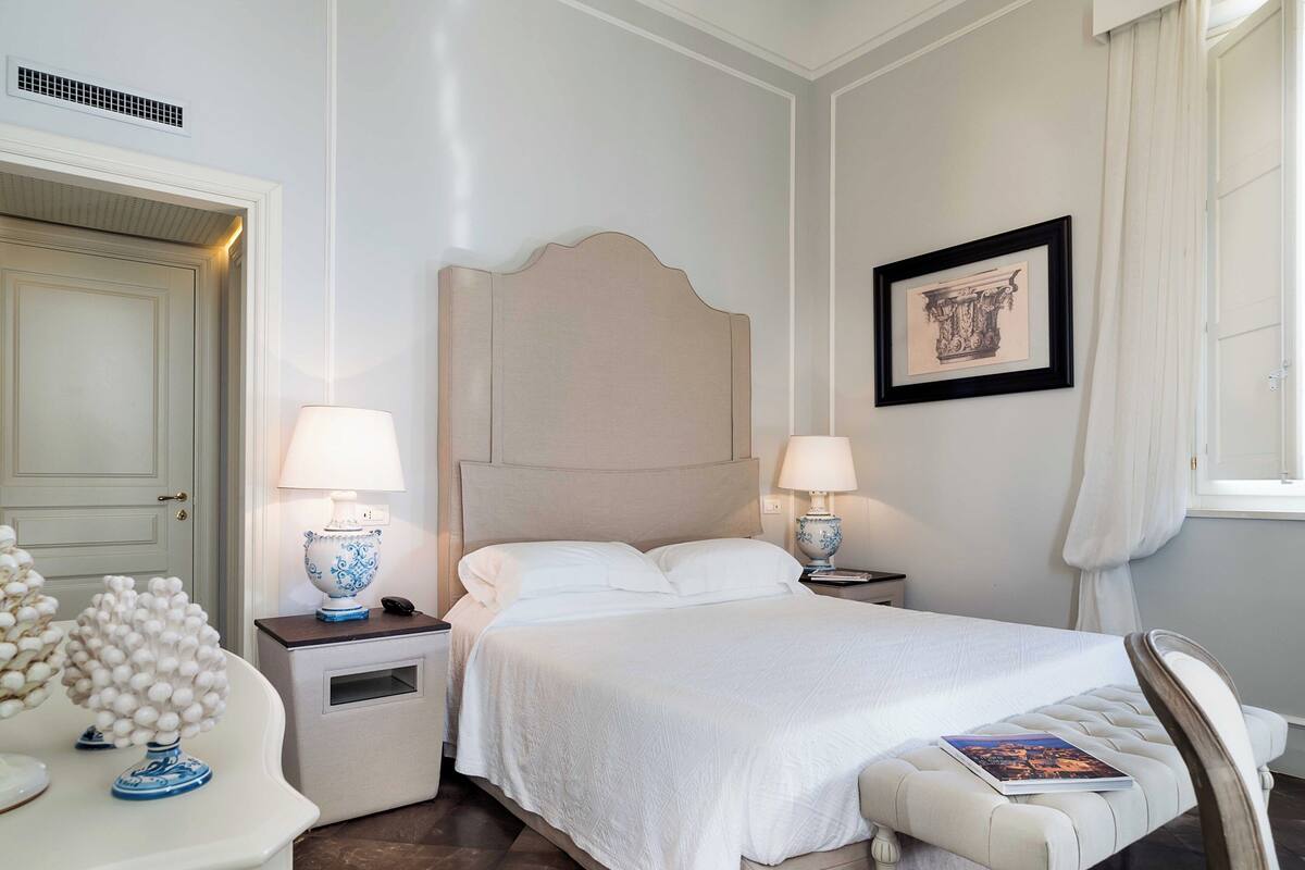 A neatly arranged hotel room with a bed, bedside tables, a chair, a decorative vase, and a framed picture on the wall.