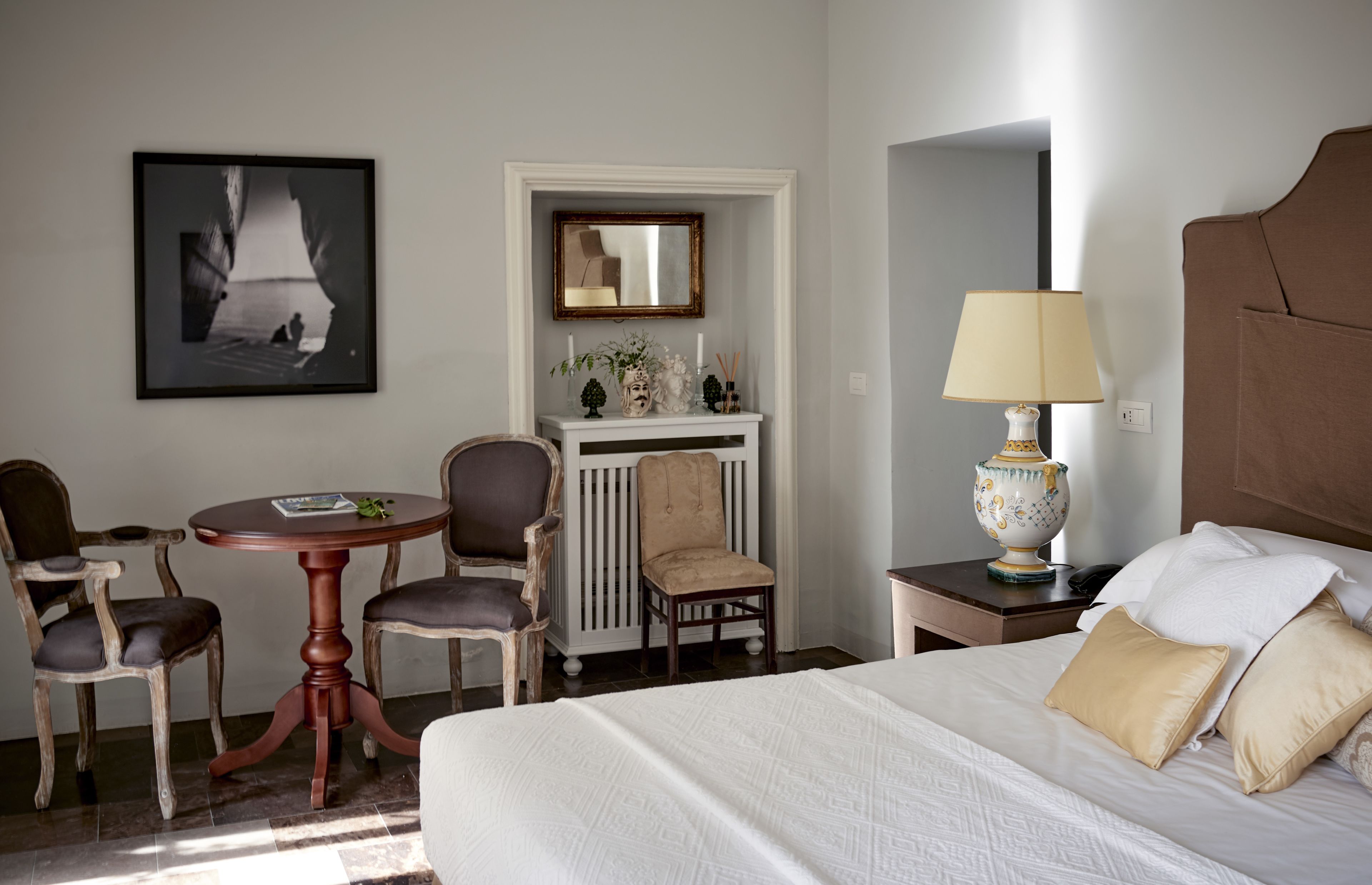 Une chambre d’hôtel avec un lit, un bureau avec deux chaises, une petite table, une lampe et un tableau encadré au mur.