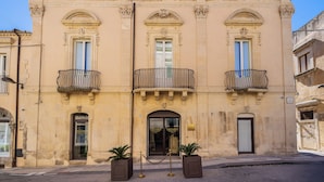 Un edificio histórico con tres balcones, una entrada central y dos macetas.