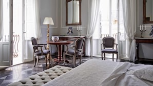 Habitación de hotel con cama, escritorio y sillas, lámpara, espejo y ventana con cortinas.