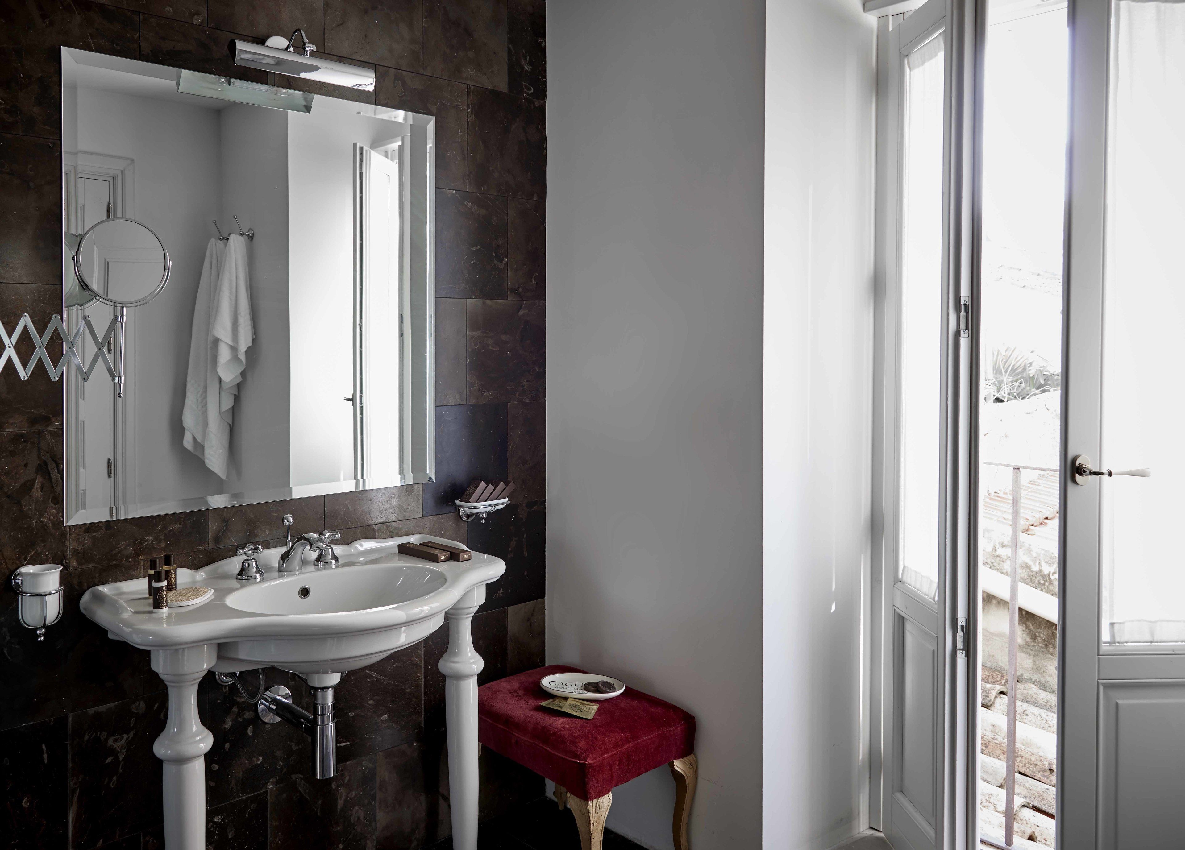 Un baño con un lavamanos blanco, un espejo y un taburete rojo.