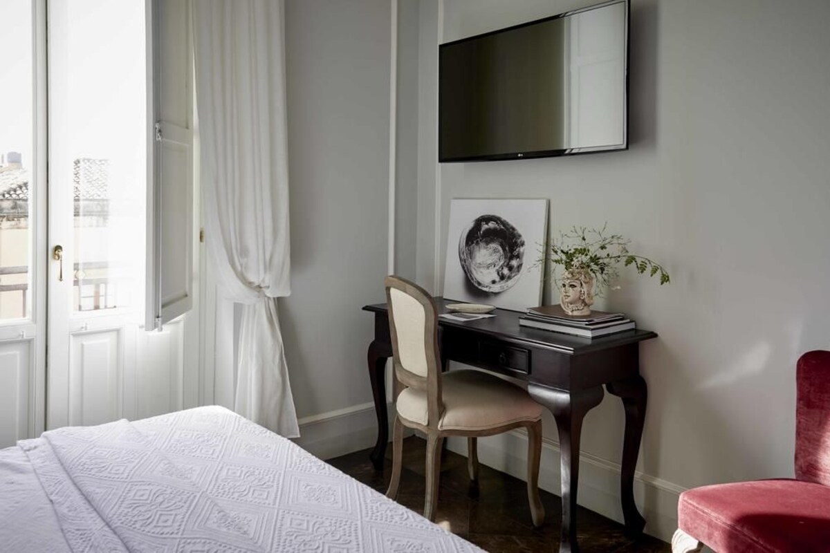 Una habitación de hotel con una cama, un escritorio con una silla, un televisor en la pared y una ventana con cortinas.