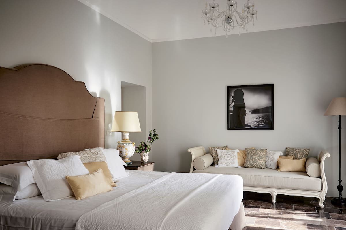 A bedroom with a large bed, a sofa, a chandelier, and a framed picture on the wall.