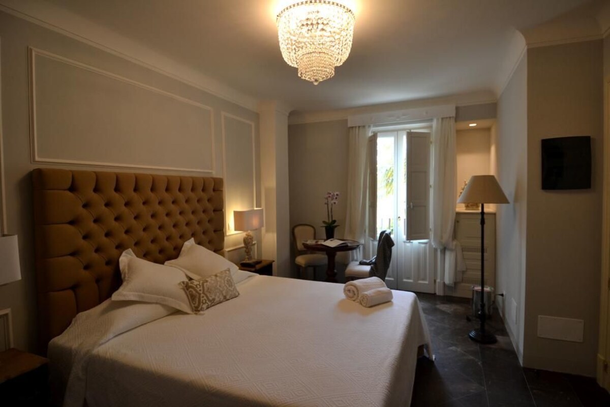 A hotel room with a large bed, a chandelier, a desk, and a chair.