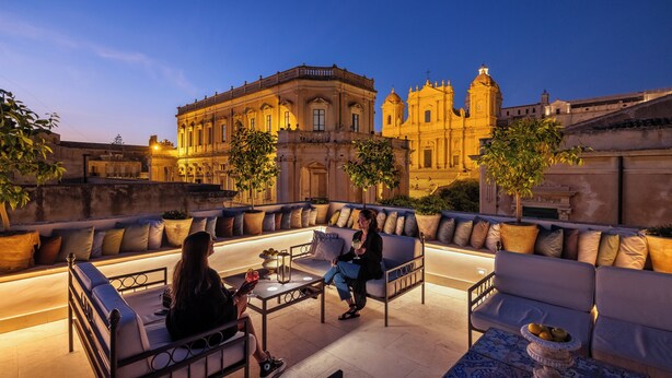 Una terraza en la azotea con mobiliario exterior, vistas a un edificio histórico y un ambiente luminoso.