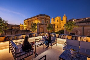 A rooftop terrace with outdoor seating, a view of a historic building, and a well-lit ambiance. - Gagliardi Boutique Hotel (Noto)