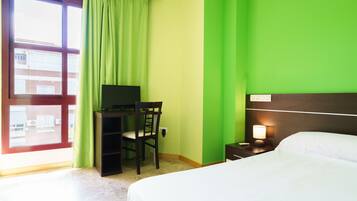 Een hotelkamer met een bed, een bureau met stoel, een televisie en een nachtkastje met lamp.