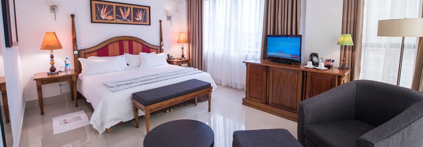 A hotel room with a bed, bedside tables, a television, a sofa, and a desk with a lamp.