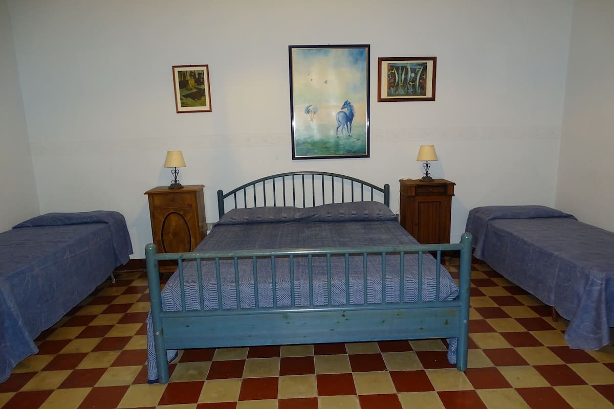 Una habitación con una cama individual, dos mesitas de noche y dos lámparas fijadas a la pared. Hay tres cuadros enmarcados en la pared.