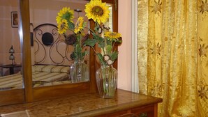 Ein hölzerner Kommode mit Spiegel, eine Vase mit Sonnenblumen und ein Bett mit Kopfteil im Hintergrund.
