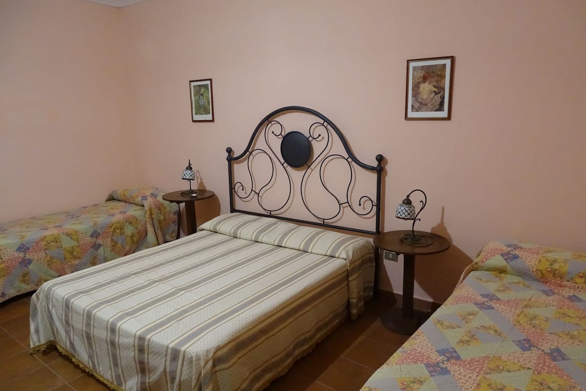 Un dormitorio con dos camas individuales, una cama grande y dos mesitas de noche con lámparas.