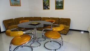Ein Zimmer mit einem runden Tisch, vier Stühlen und einem Sofa. An der Wand hängen drei gerahmte Bilder.