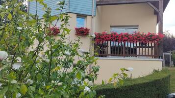 Una casa de dos plantas con fachada azul, jardineras en las ventanas y un seto cuidado.