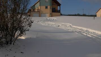 Una casa de dos pisos con un camino de entrada cubierto de nieve y un pequeño árbol en primer plano.