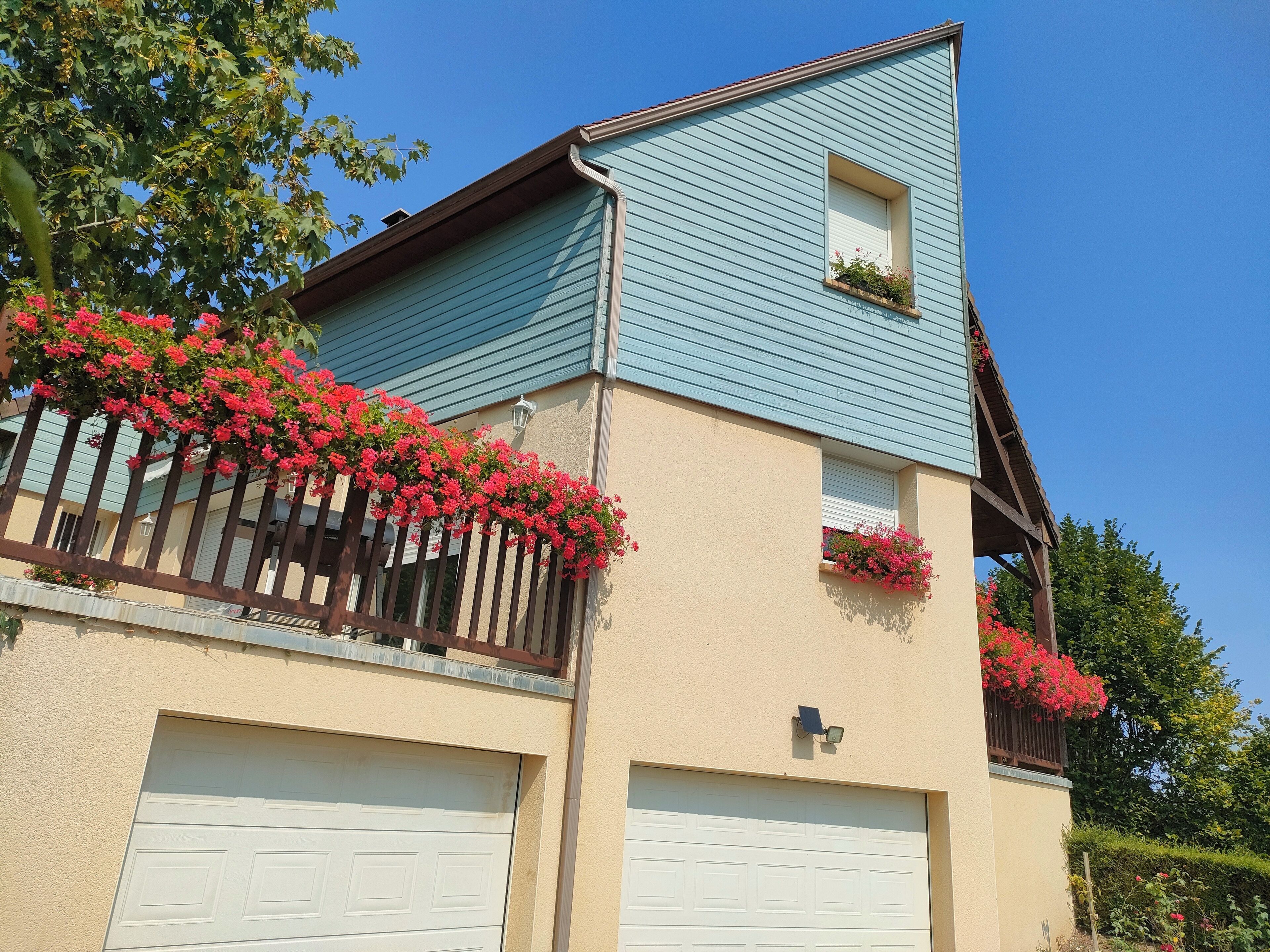 Un bâtiment à deux étages, avec une façade bleue, des portes de garage blanches et des jardinières sur le balcon.