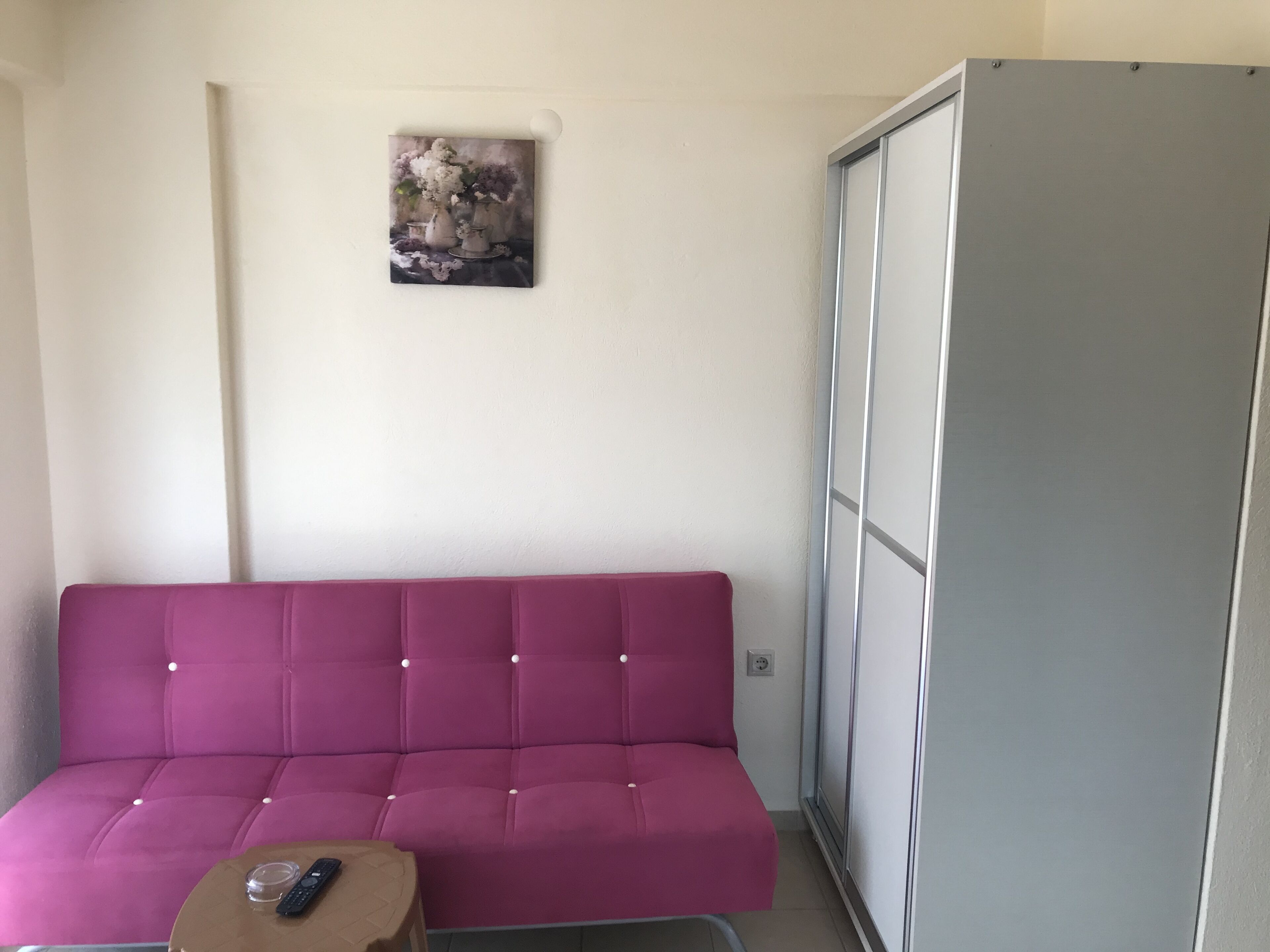 Una habitación con un sofá púrpura, una mesita con un control remoto y un armario gris.