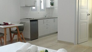 Una cocina compacta con armarios blancos, un lavamanos y una pequeña encimera. Hay una mesa de comedor con sillas y un rollo de toallas blancas en el suelo.