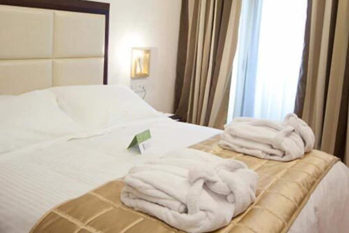 A hotel room with a bed, a nightstand, a lamp, and a window with curtains.