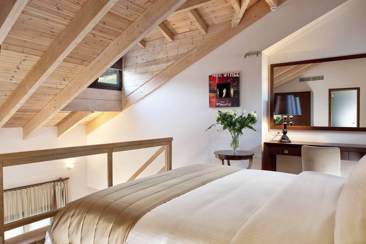 A bedroom with a sloped ceiling, a bed, a bedside table with a lamp, a mirror, and a poster on the wall.