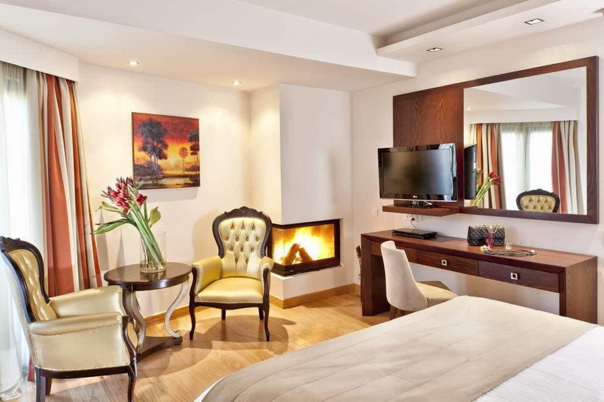 A hotel room with a bed, a seating area with a chair and a table, a fireplace, a television, and a large mirror.
