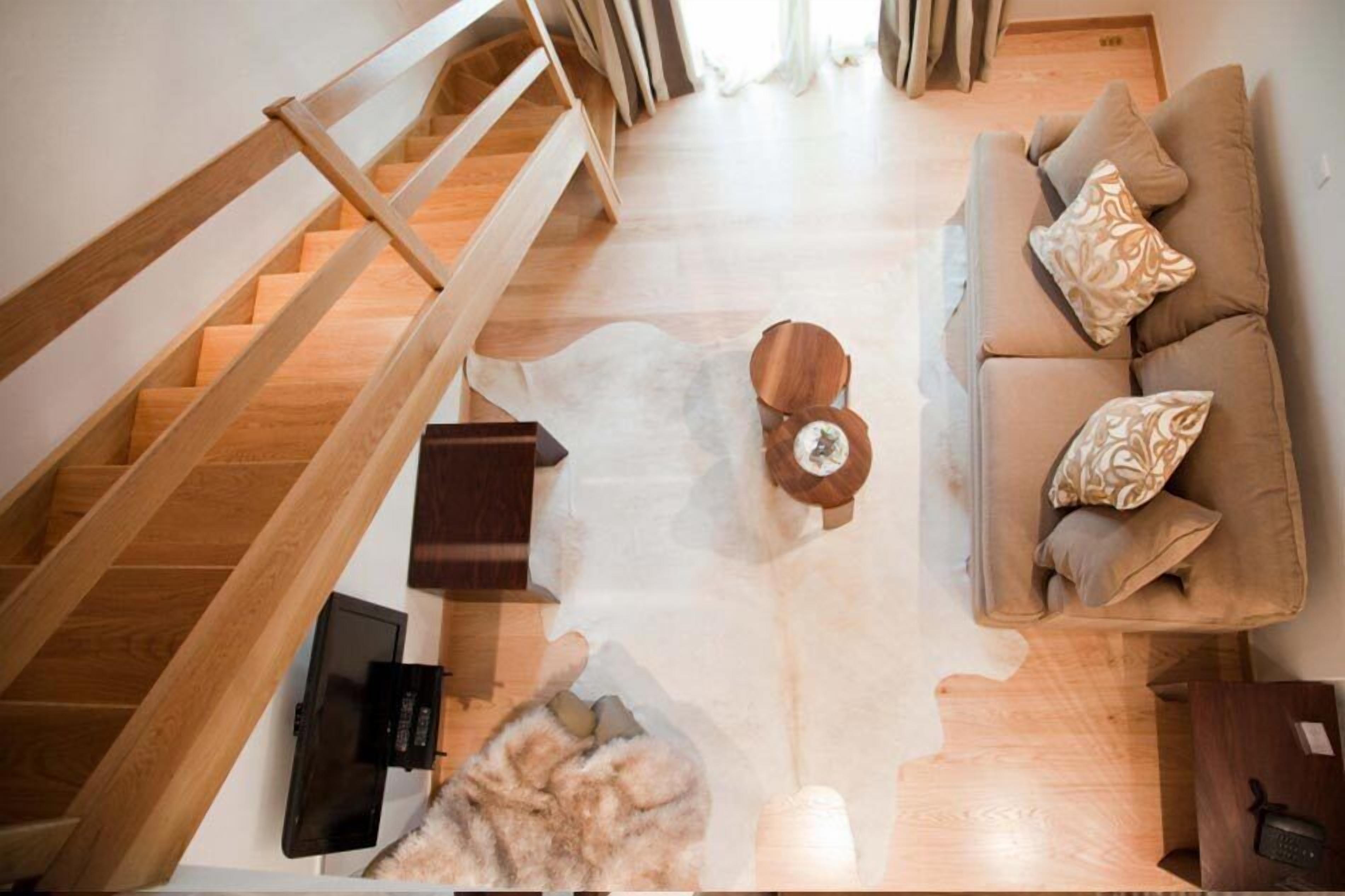 A modern living room with a wooden staircase, a sofa with patterned cushions, a round coffee table, and a fur rug.