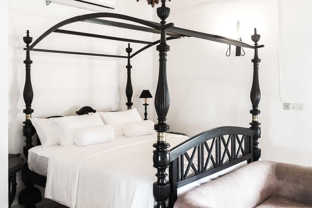 Un letto a baldacchino con struttura in legno e biancheria bianca in una stanza con soffitto in legno a falde e un lampadario.