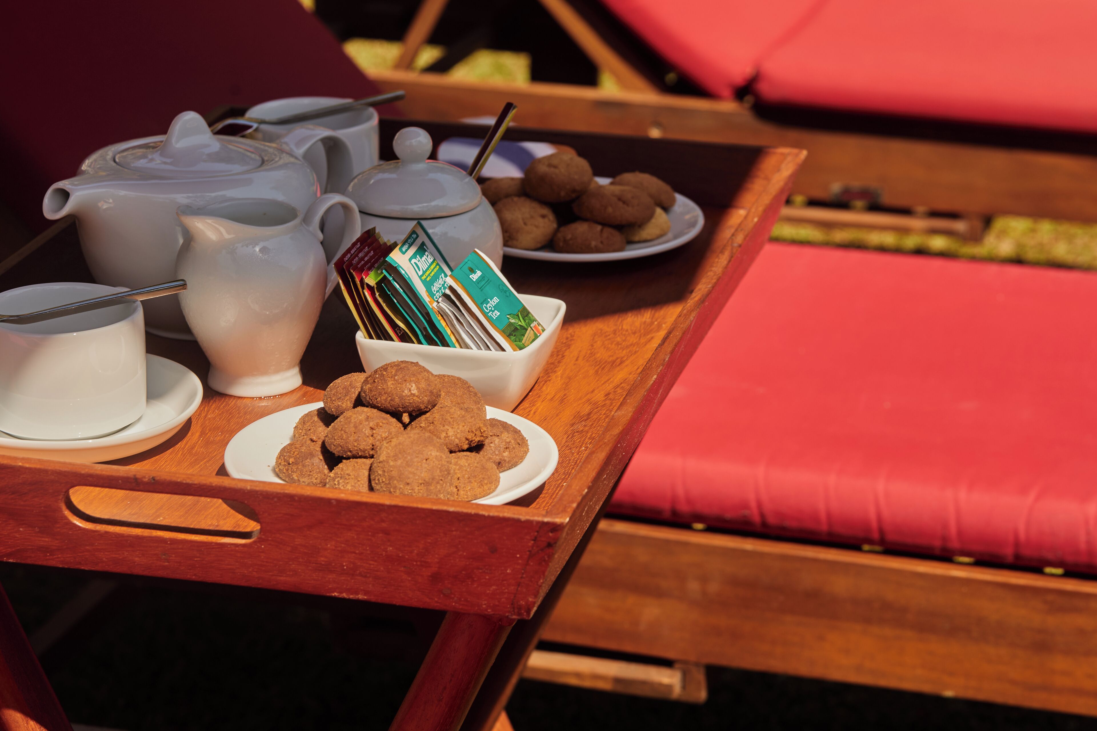 A breakfast tray with tea, coffee, cookies, and a book on a wooden table.