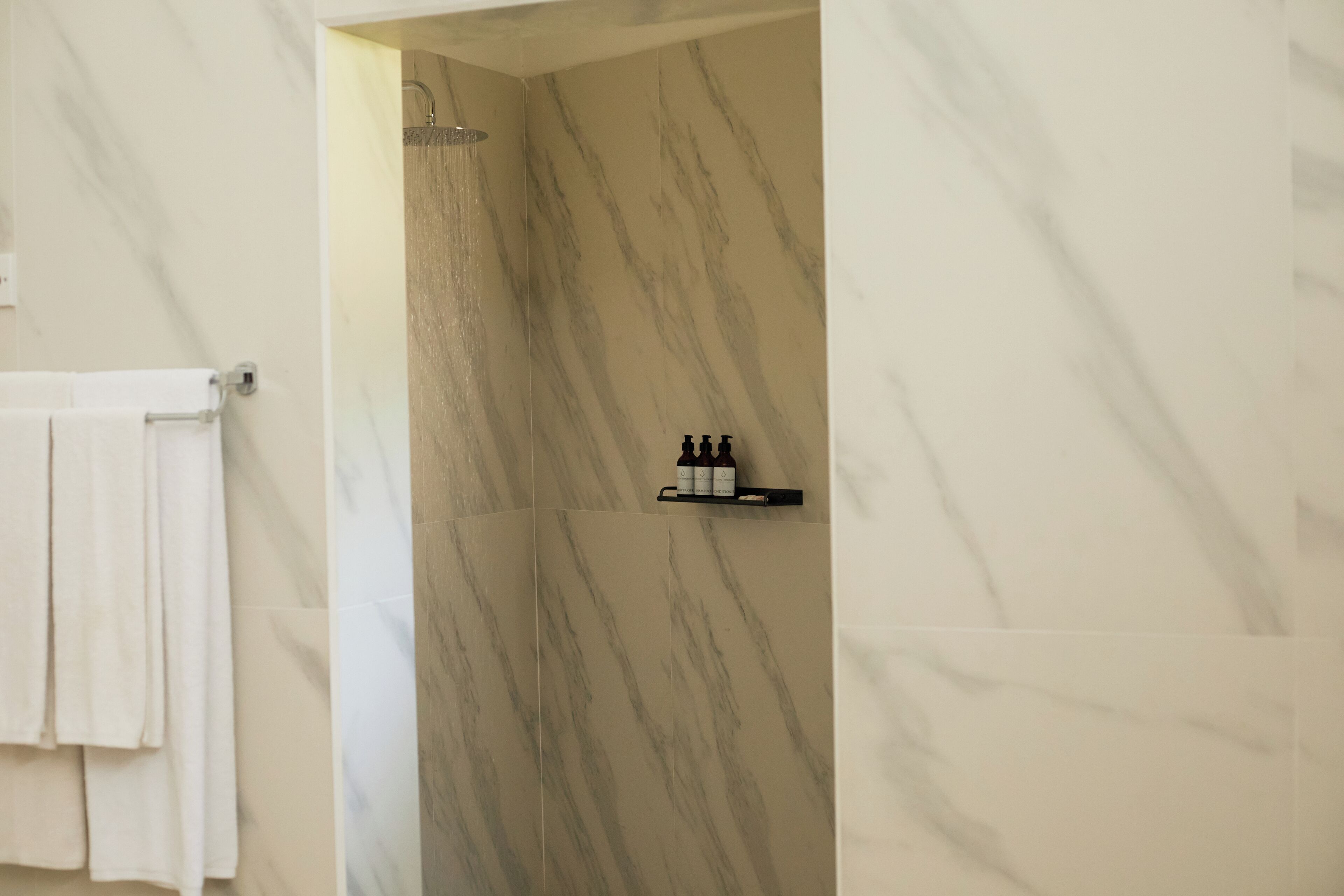 A bathroom with marble walls, a shower, and a shelf with toiletries.