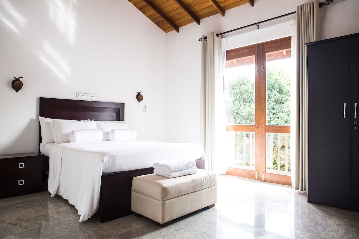 Una camera da letto con un letto, comodini, una panca, un armadio e una porta scorrevole in vetro che dà su un balcone.