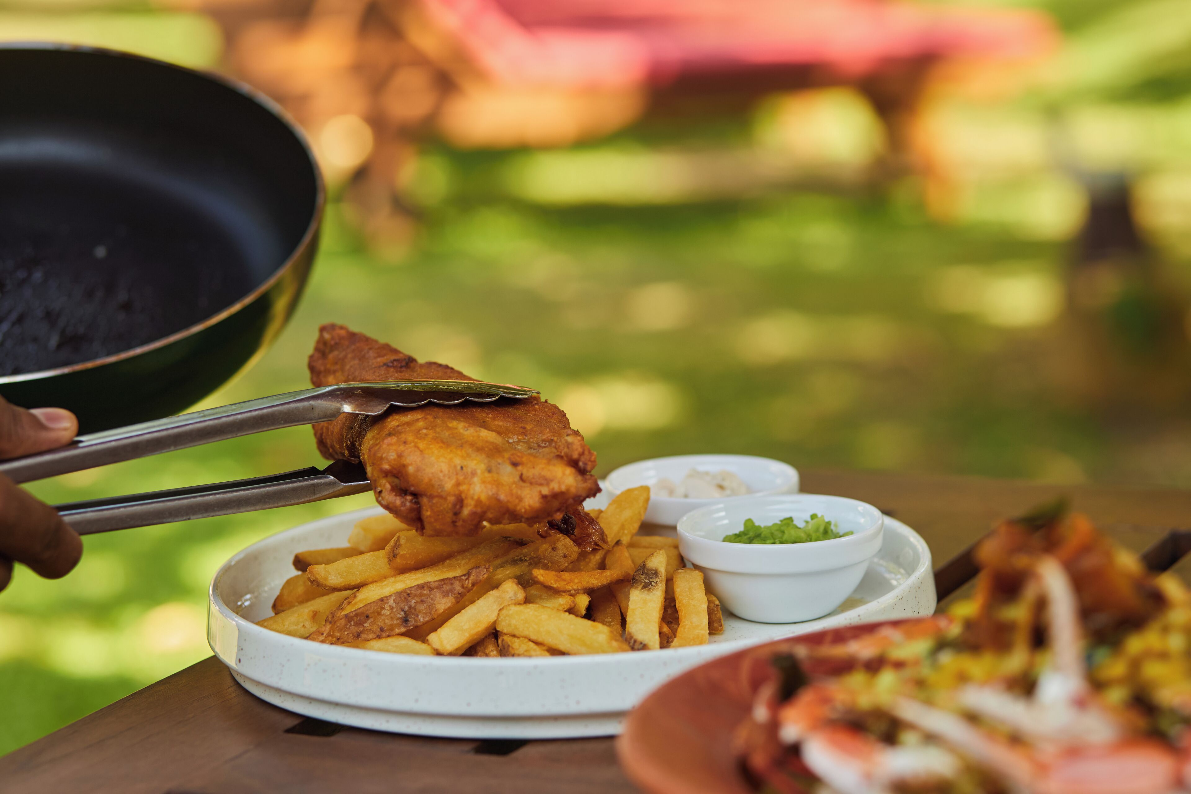 A plate of food with a fish fillet and fries, a bowl of sauce, and a bowl of salad.