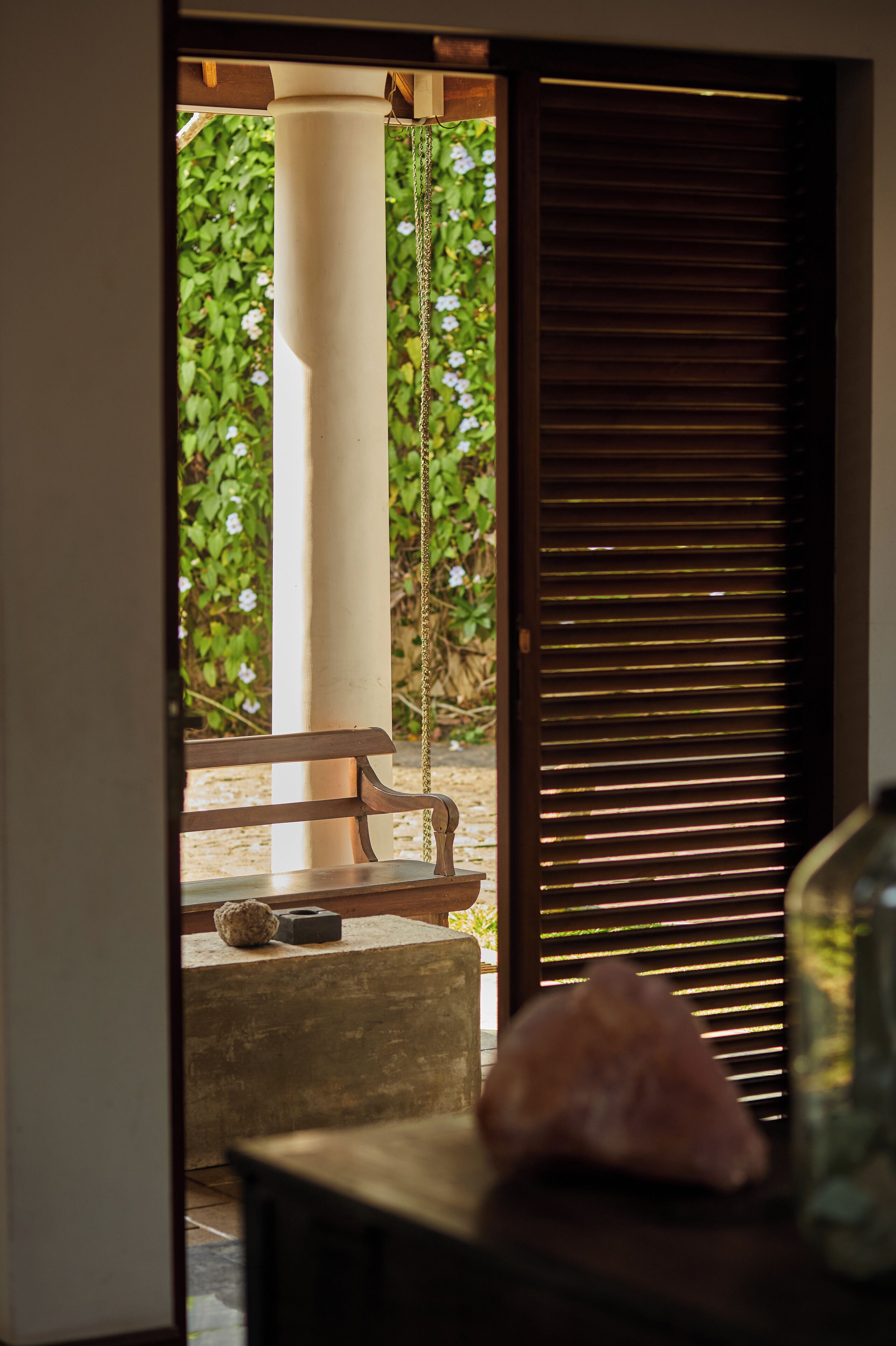 A wooden bench and a concrete block in a doorway leading to an outdoor area with a white column and a wooden shutter.