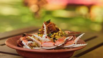 Un bol en terre cuite contenant un plat de fruits de mer composé de pattes de crabe, de maïs et d’herbes aromatiques, posé sur une table en bois.