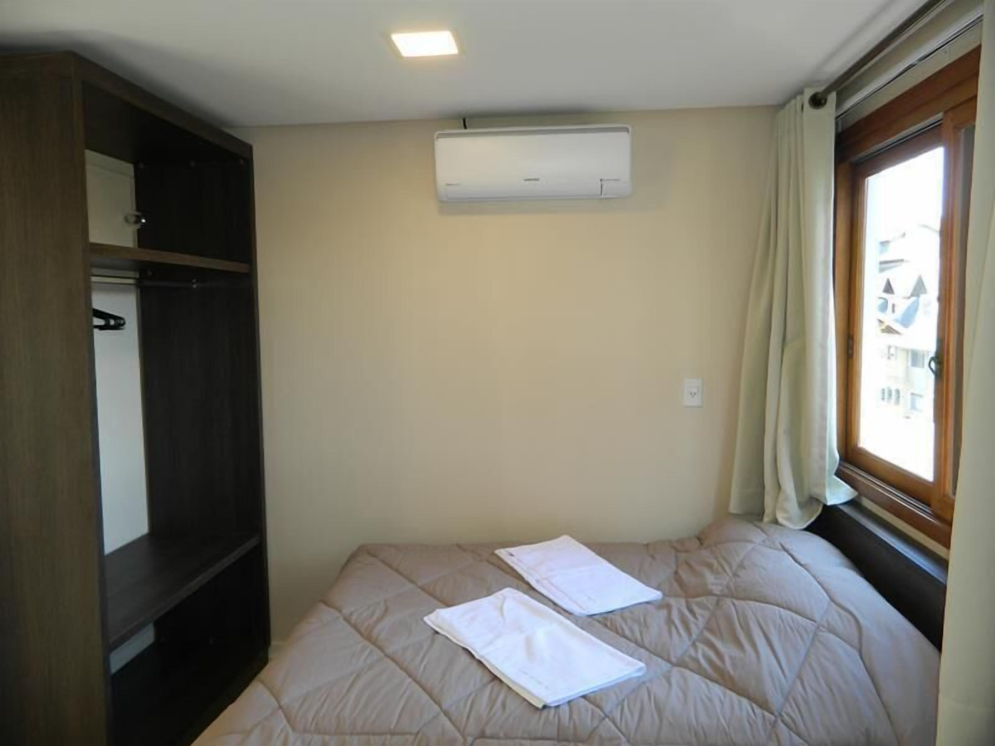 A bedroom with a bed, an air conditioner, a window with curtains, and a wardrobe.