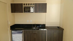 A compact kitchen with dark wood cabinets, a black countertop, a microwave, and a sink. - Residencial Maria Libardi (Gramado)