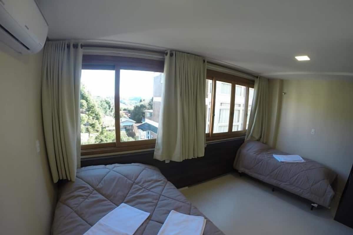 A bedroom with two beds, large windows with curtains, and an air conditioning unit.