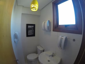 A bathroom with a toilet, sink, and a window. There is a picture on the wall and a ceiling light fixture. - Residencial Maria Libardi (Gramado)