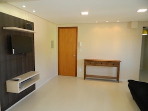A modern living room with a flat-screen TV mounted on a wooden wall, a wooden console table, and a black sofa. - Residencial Maria Libardi (Gramado)