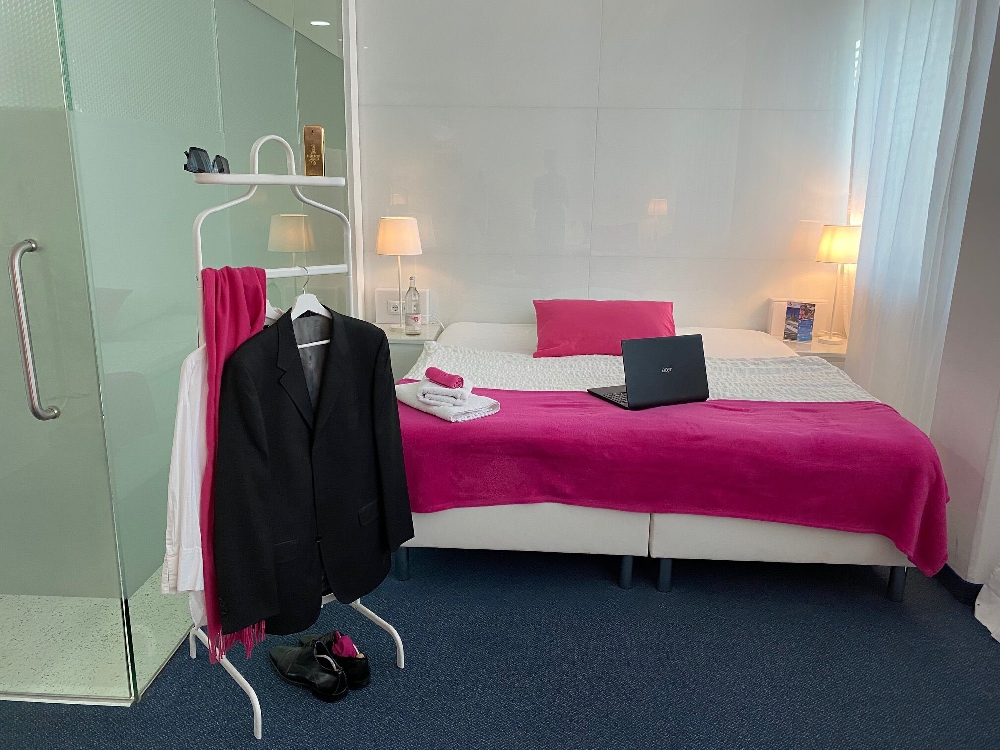 A hotel room with a bed, a laptop, a robe, and a coat rack.