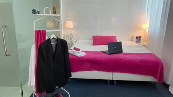 A hotel room with a bed, a laptop, a robe, and a coat rack.