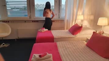A hotel room with two beds, a window with blinds, a chair, and a lamp.