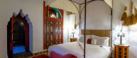 A four-poster bed with a canopy, a red armchair, a wooden cabinet with decorative panels, and a patterned floor.